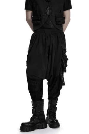 Schwarze Gothic-Haremshose mit Nieten-Cargo-Taschen, Vorderansicht-Dreiviertel-Blick auf männliches Modell mit Combat-Boots und industriellem Gothic-Stil