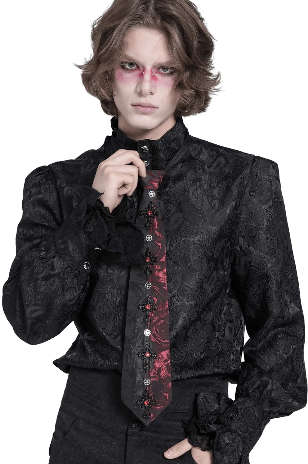 Männliches Model trägt schwarze Gothic Krawatte mit roten Rosen und Kristallkreuz mit rotem gotischem Augen-Make-up, Frontansicht auf weißem Studio-Hintergrund