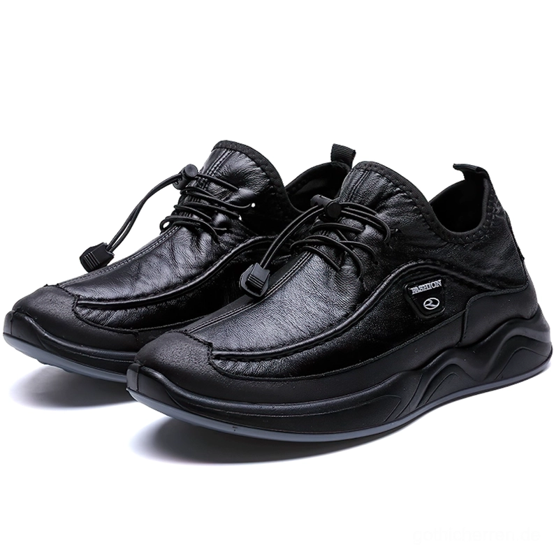 Schwarze Gothic-Ledersneaker mit adjustierbarem Toggle-Verschluss und massiver Sportlaufsohle, Vorderansicht aus drei-Viertel-Perspektive mit Studio-Hintergrund