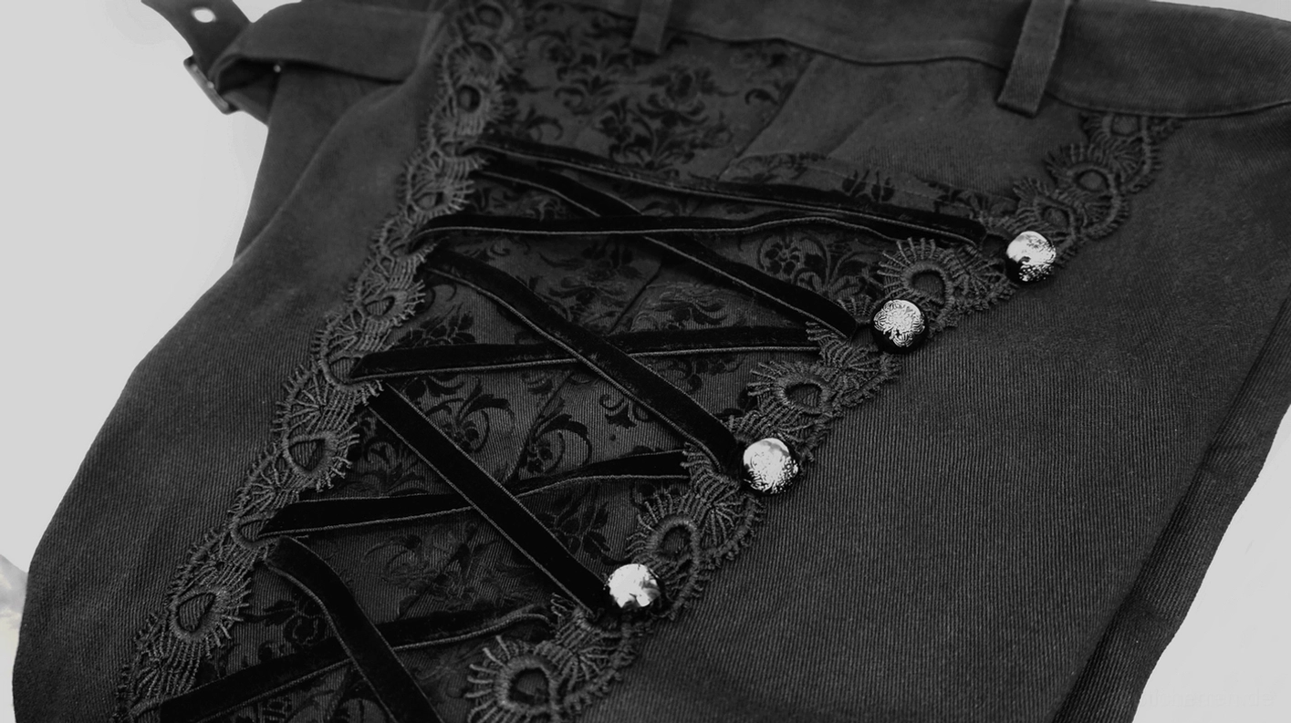 Detailaufnahme der Seitenschnürung an schwarzer Gothic-Röhrenhose mit gekreuzten Metallnieten, korsettinspirierte Schnürdetails mit dekorativen Metallfastenern und floralem Spitzenpaneel