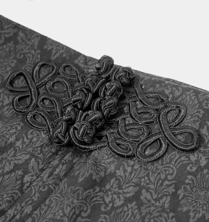 Nahaufnahme der schwarzen Gothic Röhrenhose zentraler Vorderseite mit kunstvoll besticktem chinesischem Knoten-Dekorationsmuster auf dunklem gewebtem Damast-Jacquard-Stoff auf weißem Hintergrund