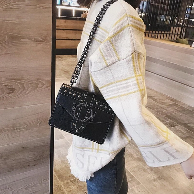 Frau trägt schwarze Gothic Quadrat-Schultertasche als Crossbody-Umhängetasche, seitliche Ansicht in urbaner Umgebung mit Holzboden, kompakte Größe und Tragekomfort demonstriert