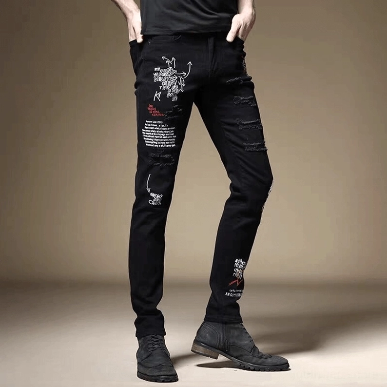 Schwarze Gothic-Slim-Jeans Seitenansicht auf männlichem Model, zeigt Graffiti-Buchstaben-Drucke und zerstörte Details mit schlanker Passform und kantigem Punk-Aesthetic