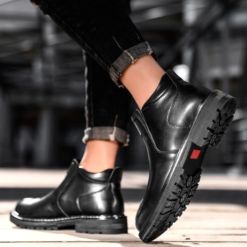 Mann zeigt schwarze Gothic Leder-Knöchel-Stiefel mit strukturierter rutschfester Sohle, urbane Außenszenerie, Detail der Sohlenstruktur und Verarbeitung