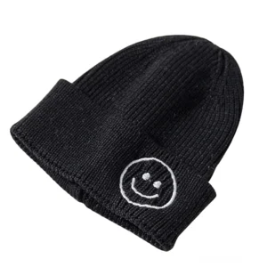Schwarze gerippte Strickmütze mit weiß gesticktem Smiley-Gesicht, Gothic Winterbeanie mit Stickerei-Detail auf weißem Hintergrund, obere Schrägansicht