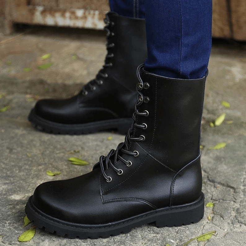 Schwarze Lace-Up Combat Boots gestylt am Modell, Vorne-Seite mit blauen Jeans, Round-Toe und matter schwarzer Lederoberfläche, Outdoor mit Blättern