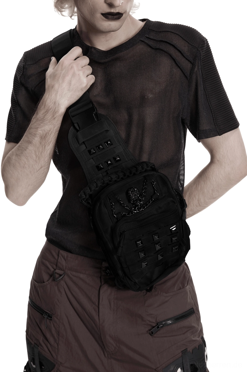 Schwarze Skull-Nieten Gothic Umhängetasche auf männlichem Model mit dunklem alternativem Outfit – Frontansicht mit Totenkopf-Hardware und pyramidenförmigen Nieten