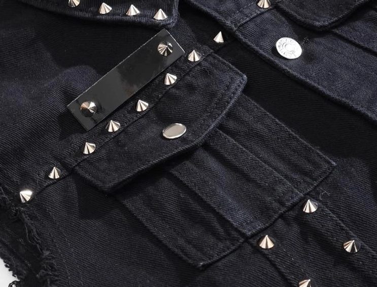 Angewinkelte Nahaufnahme der schwarzen Denim Weste Taschenkante mit silbernen Spike-Nieten und Metallbefestigungen, Pattentaschen-Detail, gotischer Style