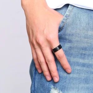 Schwarzer Gothic Groove Ring am Zeigefinger eines Mannes mit blauer Jeans im Hintergrund, Close-up Detailansicht, alternative Schmuckstil