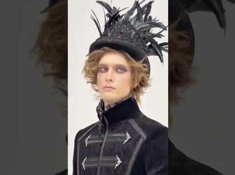 Männliches Model trägt schwarzen gotischen Federzylinder mit formalem dunklem Mantel mittlere Aufnahme zeigt komplettes Styling Ensemble