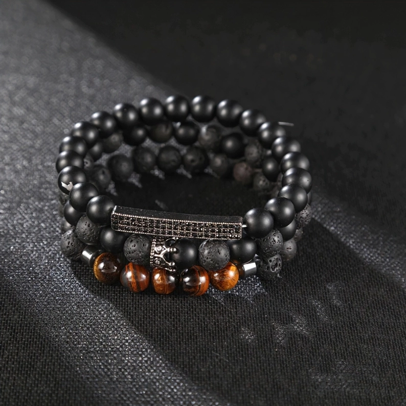 Schwarzes Onyx Gothic-Armband Flatlay-Fotografie zeigt gravierte Metallplatte und Kronenverzierung, dunkler Stoff-Hintergrund hebt die Schmuck-Details hervor