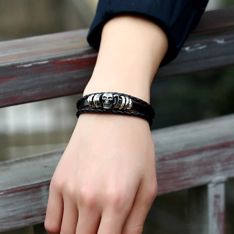 Schwarzes Gothic Schädel Armband getragen am Handgelenk Seitenansicht im Freien zeigt Seitenprofil und silberne Metalldetails auf natürlichem Holzhintergrund