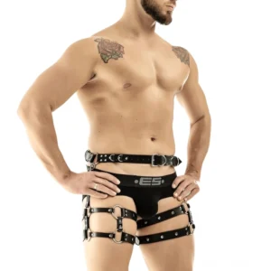 Schwarzes Kunstleder-Oberschenkel-Taille-Harness für Männer mit Metallbeschlägen, Frontansicht auf tätowiertem männlichem Model, weißer Studiohintergrund, verstellbare Schnallen und D-Ringe, Industrial-Goth-Ästhetik