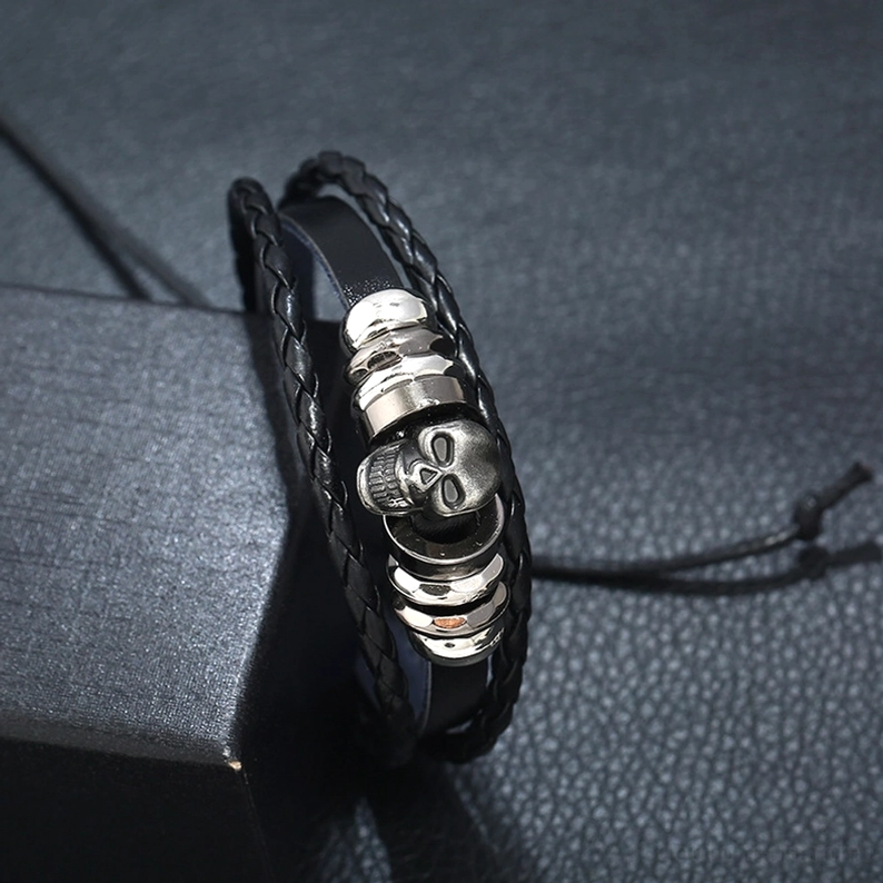 Nahaufnahme Detail des Gothic Schädel Armband-Mittelpunkts zeigt versilbertes Schädel-Charm, gestapelte Metallscheiben und kunstvolles geflochtenes Lederkanten-Handwerk