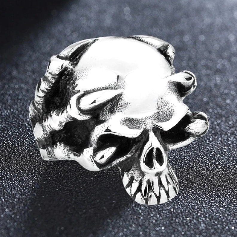 Polierter Edelstahl-Totenkopf-Ring Seitenprofil auf dunkelm Hintergrund, zeigt den glänzenden Metallfinish und skelettalen Krallenkonturen in dramatischem Licht gotische Statement-Ware