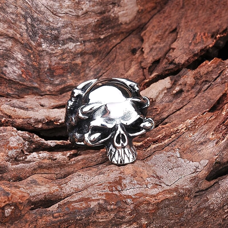 Flachwinkel-Vorderansicht silberner Totenkopf-Krallen-Ring auf Holzhintergrund, kompaktes Skelettring-Design mit schützenden seitlichen Klauen-Details und poliertem Glanz