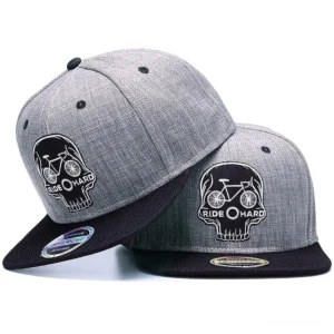 Zwei identische Skull Ride Hard Gothic Snapback Kappen in doppelter Ansicht, zeigt Heather-Grau-Krone mit schwarzem besticktem Totenkopf-Fahrrad-Motiv und RIDE HARD Schriftzug auf 6-Panel Baseball-Kappe mit flacher schwarzer Krempe