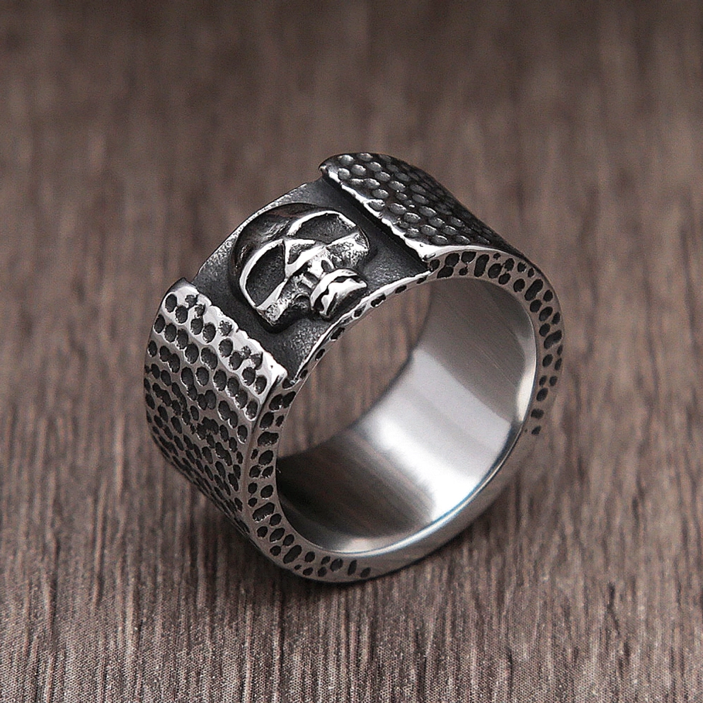Cross-eyed skull biker ring 3/4 side view displaying embossed metalwork texture and dark silver finish on wood background