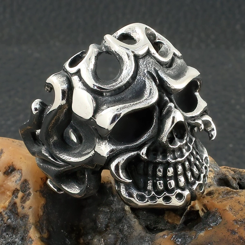 Nahaufnahme vorne des gealter Silber Skull Edelstahlring mit schwarzer Patina auf Gesteinstextur-Hintergrund, zeigt detaillierte Tribal-Hohlmuster und Gothic-Ornamente
