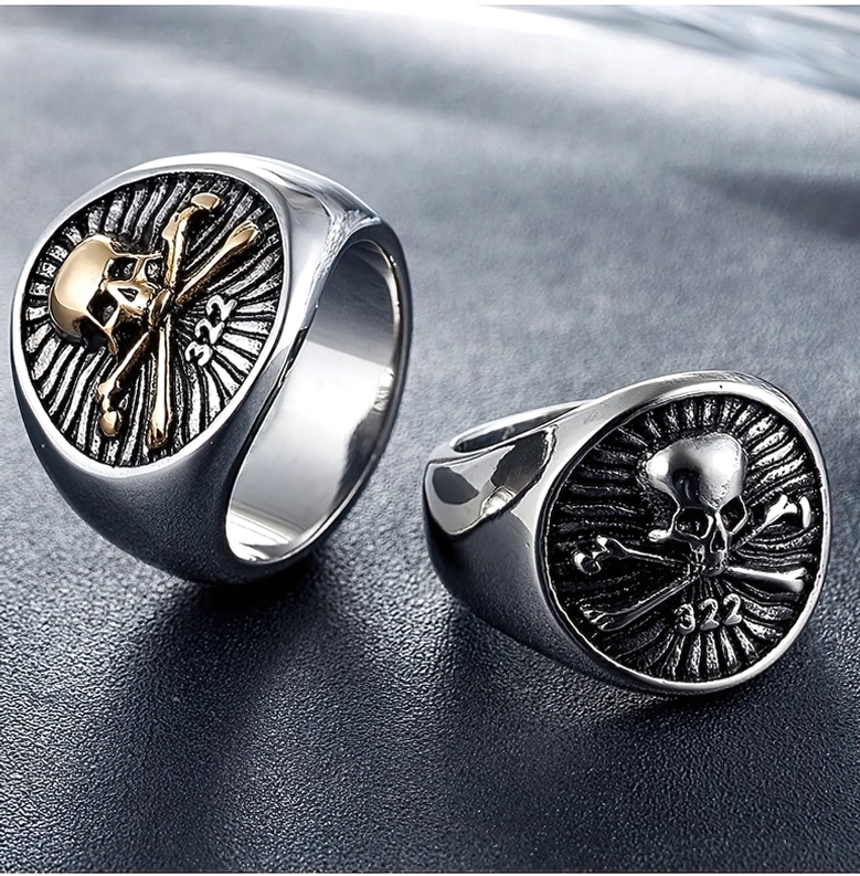 Paar Totenkopf Piraten-Sigelringe in Silber und Gold, Aufsicht auf dunklem Lederhintergrund im gotischen Stil