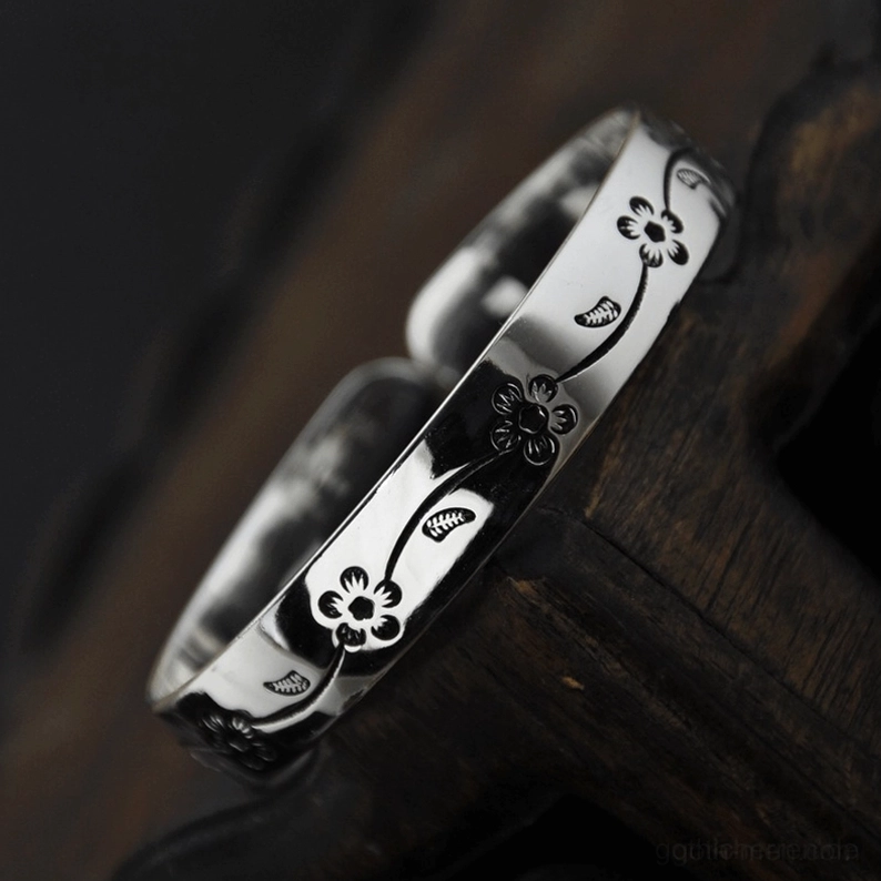 Vintage-Blüten-Manschetten-Armband mit oxidierter dunkler Gravur auf retro-Silber-Finish, Nahaufnahme Seitenansicht auf Holz-Hintergrund