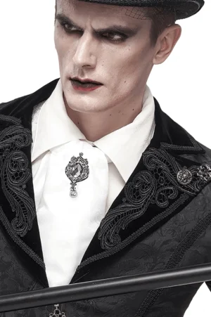 Männlicher Gothic-Performer trägt weiße Gothic-Krawatte mit Kristallbrosche und schwarz besticktem formalen Anzug – viktorianischer Stil mit dunklem Make-up und Zylinder