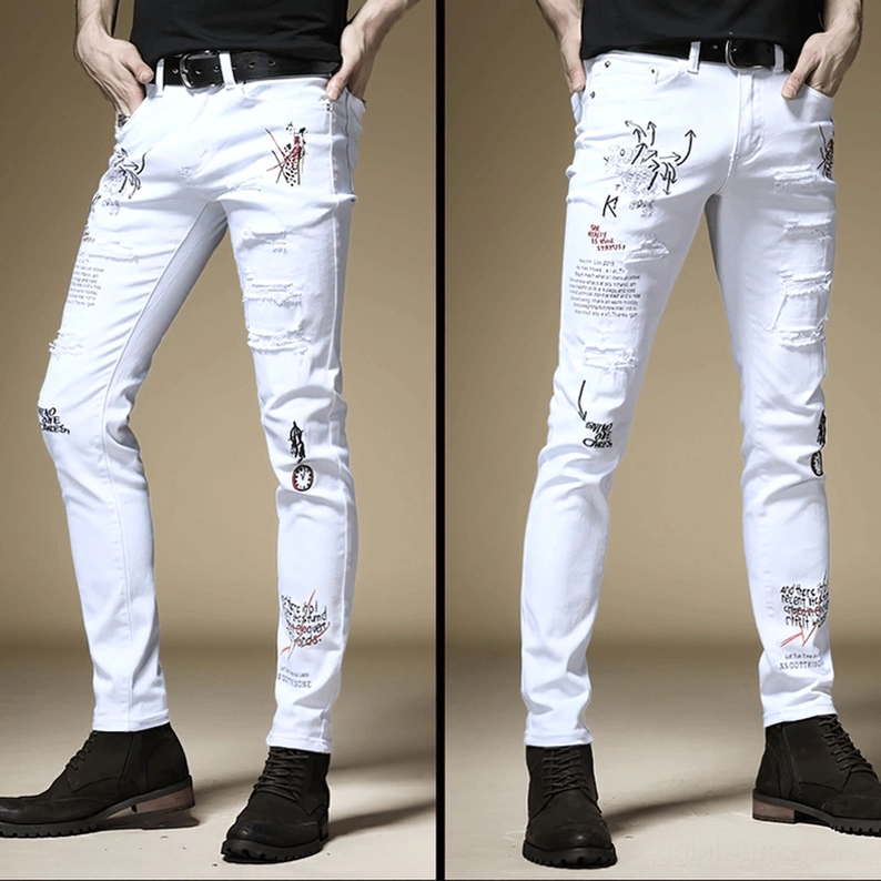 Weiße Gothic-Slim-Jeans Vorderseite Seitenansicht auf männlichem Model, zeigt Graffiti-Buchstaben-Drucke und zerstörte Löcher mit schlanker weißer Denim-Silhouette und alternativer Mode-Ästhetik